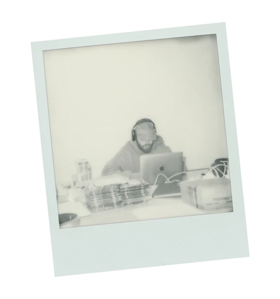 Polaroid of a sound engineer wearing headphones, seated at a mixing board in a recording studio with professional audio equipment.
